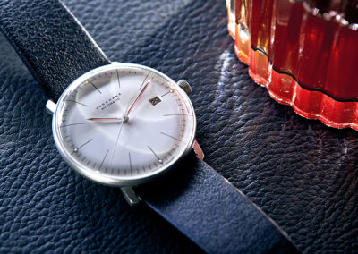 Junghans Bauhaus Uhr mit roten Zeigern liegt neben einem Glas